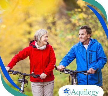 An older man and woman in red and blue jackets walk with bicycles on a tree-lined path. The Aquileg logo is at the corner.