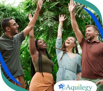Four people stand outdoors in front of greenery, smiling and raising one hand each. The Aquileg logo is visible in the bottom right corner.