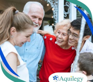 Four people of different ages stand close together, smiling and embracing outdoors. The Aquilegy logo is visible in the bottom right corner.